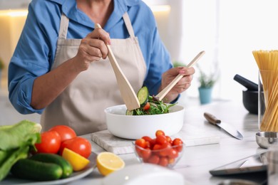 Photo of Senior woman cooking salad at white marble table in kitchen, closeup