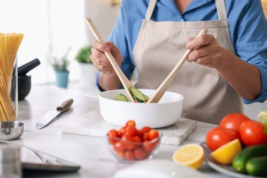 Photo of Senior woman cooking salad at white marble table in kitchen, closeup