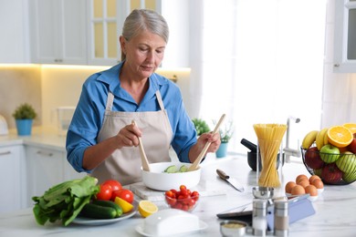 Photo of Senior woman cooking salad at white marble table in kitchen