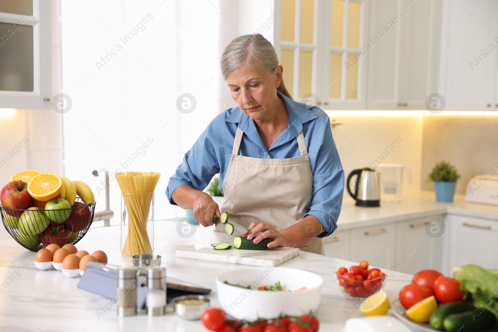 Senior woman cooking at white marble table in kitchen Photo of Senior woman cooking at white marble table in kitchen