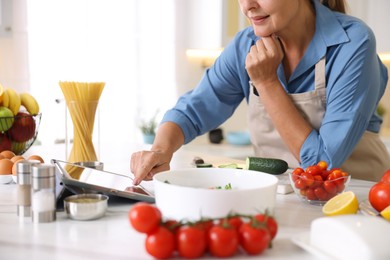 Photo of Senior woman using tablet while cooking at white marble table in kitchen, closeup