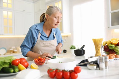 Photo of Senior woman using tablet while cooking at white marble table in kitchen