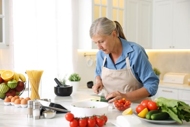 Photo of Senior woman cooking at white marble table in kitchen