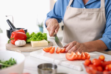 Photo of Senior woman cooking at white marble table in kitchen, closeup
