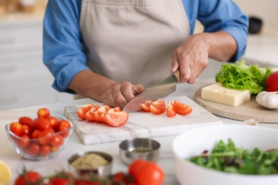 Photo of Senior woman cooking at white marble table in kitchen, closeup
