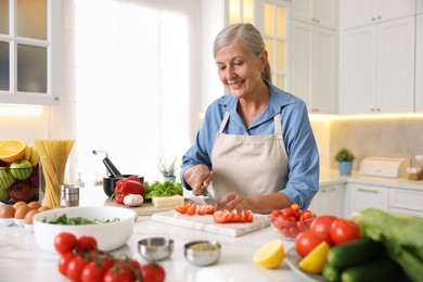 Photo of Senior woman cooking at white marble table in kitchen