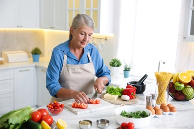 Photo of Senior woman cooking at white marble table in kitchen