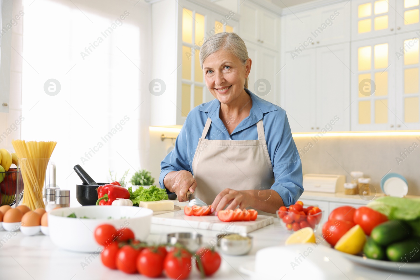 Senior woman cooking at table in kitchen Photo of Senior woman cooking at table in kitchen