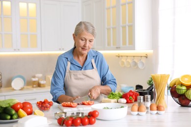 Photo of Senior woman cooking at white marble table in kitchen