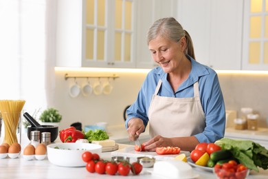 Photo of Senior woman cooking at white marble table in kitchen