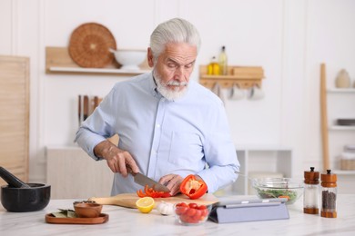 Photo of Elderly man cooking at white marble table in kitchen