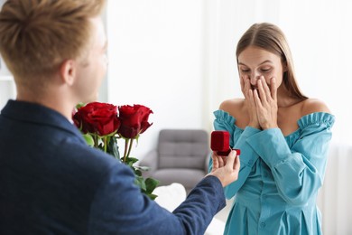 Photo of Man with engagement ring and bouquet of roses making marriage proposal to his happy girlfriend at home