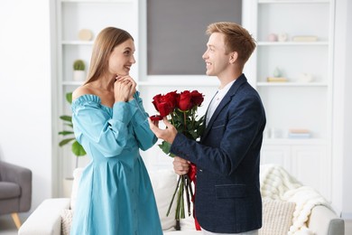 Photo of Man with engagement ring and bouquet of roses making marriage proposal to his happy girlfriend at home