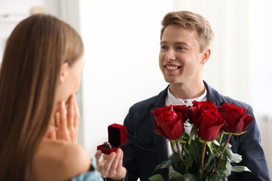 Photo of Smiling man with engagement ring and bouquet of roses making marriage proposal to his girlfriend at home