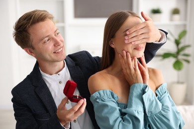 Photo of Making marriage proposal. Smiling man with engagement ring surprising his girlfriend at home