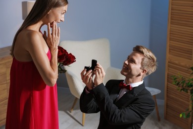 Photo of Smiling man with engagement ring making marriage proposal to his excited girlfriend at home