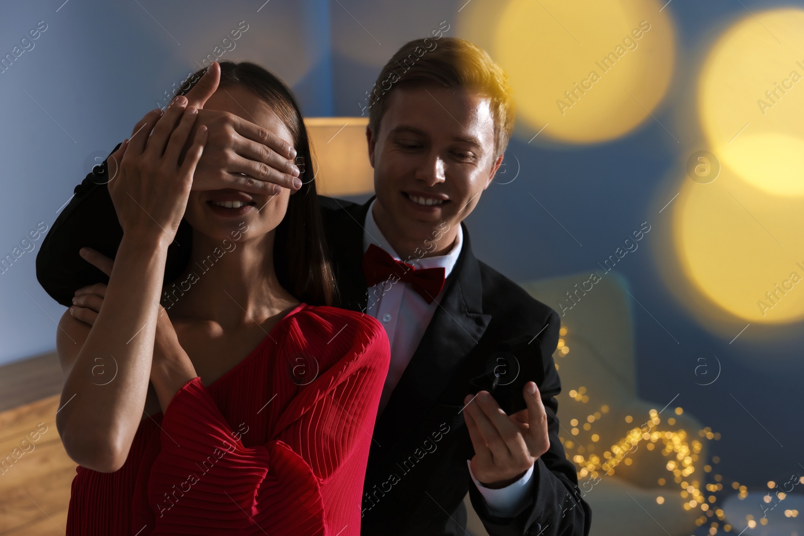 Making marriage proposal. Smiling man with engagement ring surprising his girlfriend in dark room. Bokeh effect Photo of Making marriage proposal. Smiling man with engagement ring surprising his girlfriend in dark room. Bokeh effect