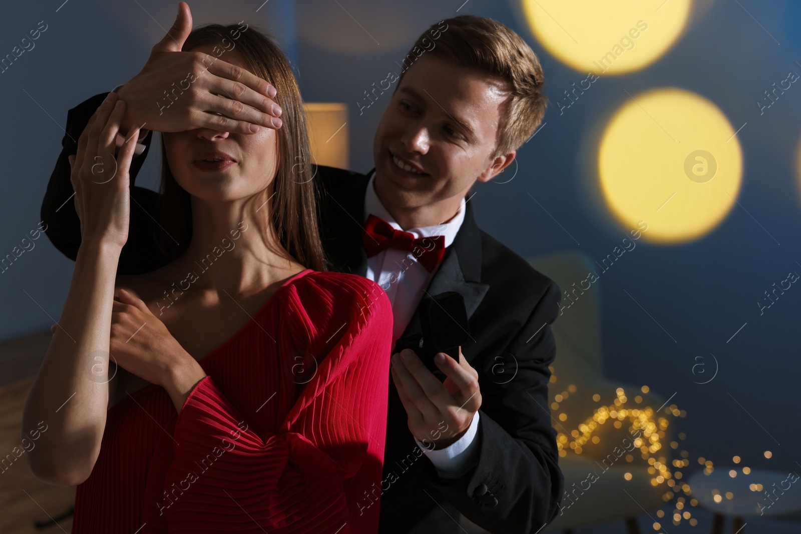 Making marriage proposal. Smiling man with engagement ring surprising his girlfriend in dark room. Bokeh effect Photo of Making marriage proposal. Smiling man with engagement ring surprising his girlfriend in dark room. Bokeh effect