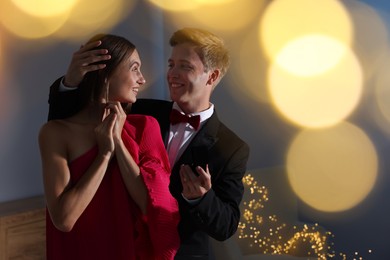 Photo of Making marriage proposal. Smiling man with engagement ring surprising his girlfriend in dark room, space for text. Bokeh effect