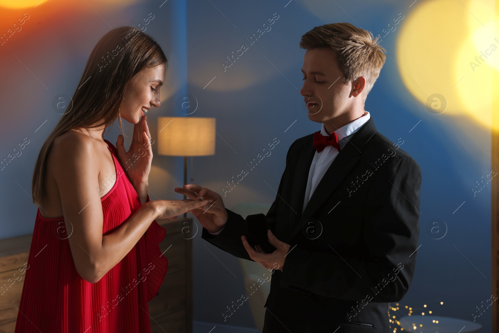 Making marriage proposal. Man putting engagement ring onto his girlfriend's finger in dark room. Bokeh effect Photo of Making marriage proposal. Man putting engagement ring onto his girlfriend's finger in dark room. Bokeh effect