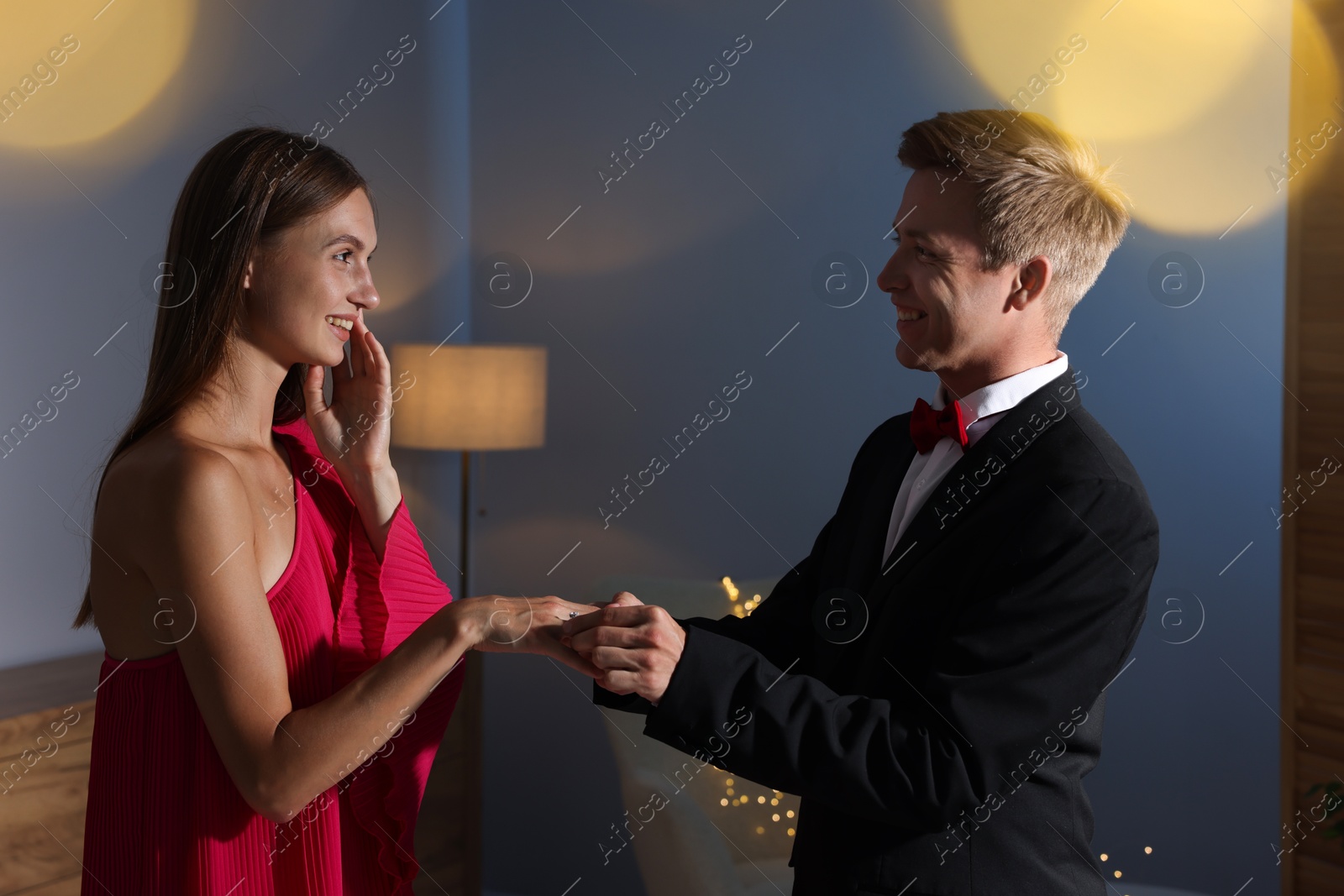 Making marriage proposal. Smiling man putting engagement ring onto his girlfriend's finger in dark room. Bokeh effect Photo of Making marriage proposal. Smiling man putting engagement ring onto his girlfriend's finger in dark room. Bokeh effect