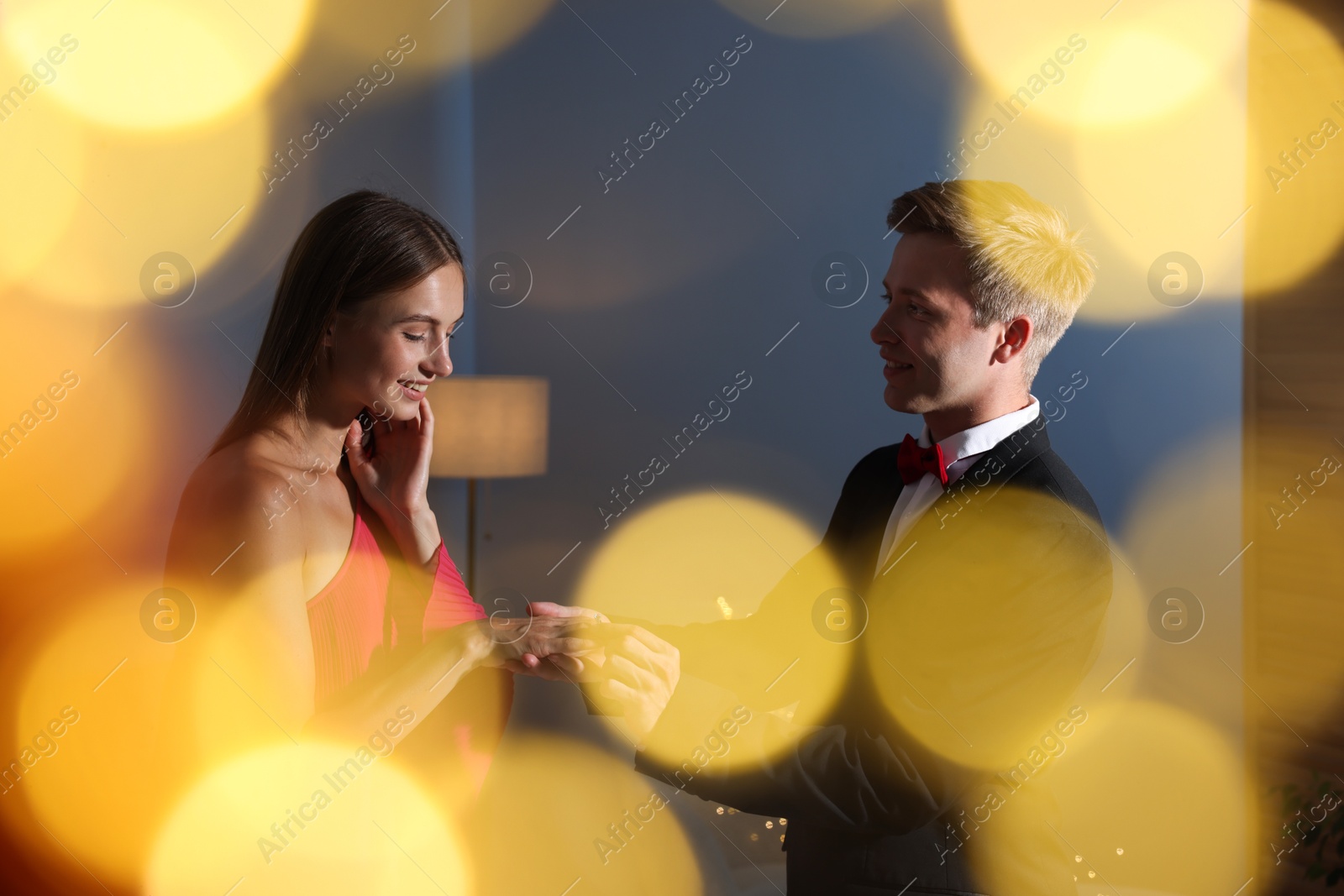 Making marriage proposal. Smiling man putting engagement ring onto his girlfriend's finger in dark room. Bokeh effect Photo of Making marriage proposal. Smiling man putting engagement ring onto his girlfriend's finger in dark room. Bokeh effect