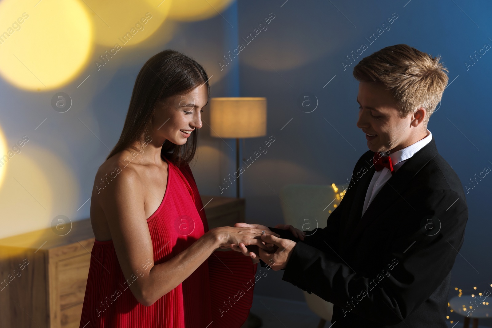 Making marriage proposal. Smiling man putting engagement ring onto his girlfriend's finger in dark room. Bokeh effect Photo of Making marriage proposal. Smiling man putting engagement ring onto his girlfriend's finger in dark room. Bokeh effect