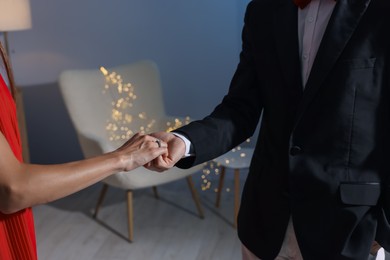 Photo of Making marriage proposal. Woman with engagement ring and her fiance holding hands at home, closeup. Bokeh effect