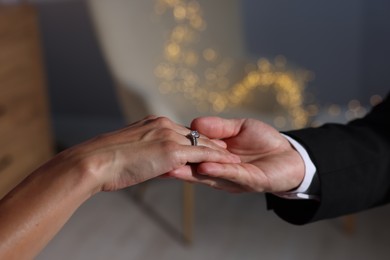 Photo of Making marriage proposal. Woman with engagement ring and her fiance holding hands at home, closeup. Bokeh effect