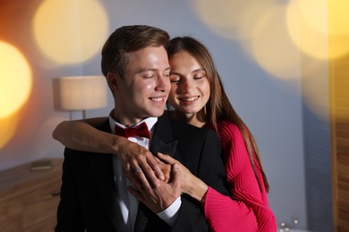 Photo of Making marriage proposal. Woman with engagement ring and her smiling fiance hugging at home. Bokeh effect