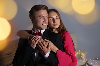 Photo of Making marriage proposal. Woman with engagement ring and her smiling fiance hugging at home. Bokeh effect