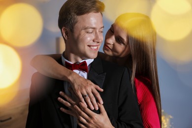 Photo of Making marriage proposal. Woman with engagement ring and her smiling fiance hugging at home. Bokeh effect
