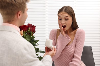 Photo of Man with engagement ring and bouquet of roses making marriage proposal to his emotional girlfriend at home