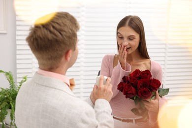 Photo of Man with engagement ring and bouquet of roses making marriage proposal to his happy girlfriend at home. Bokeh effect