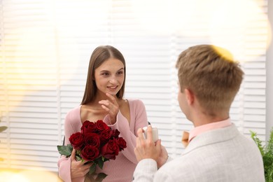 Photo of Man with engagement ring and bouquet of roses making marriage proposal to his happy girlfriend at home. Bokeh effect