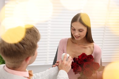 Photo of Man with engagement ring and bouquet of roses making marriage proposal to his happy girlfriend at home. Bokeh effect