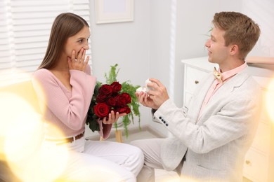 Photo of Man with engagement ring and bouquet of roses making marriage proposal to his emotional girlfriend at home. Bokeh effect
