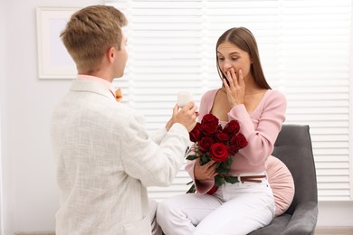 Photo of Man with engagement ring and bouquet of roses making marriage proposal to his happy girlfriend at home