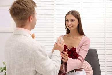 Photo of Man with engagement ring and bouquet of roses making marriage proposal to his happy girlfriend at home