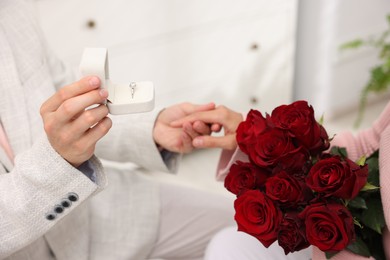 Photo of Man with engagement ring making marriage proposal to his girlfriend with bouquet of roses at home, closeup