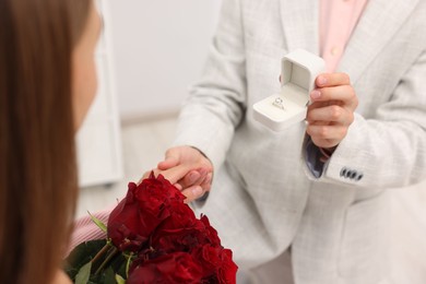 Photo of Man with engagement ring making marriage proposal to his girlfriend with bouquet of roses at home, closeup