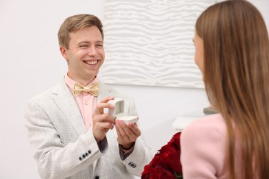 Photo of Smiling man with engagement ring making marriage proposal to his girlfriend with bouquet of roses at home