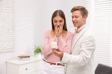 Photo of Marriage proposal. Smiling man with engagement ring and his surprised girlfriend at home, space for text