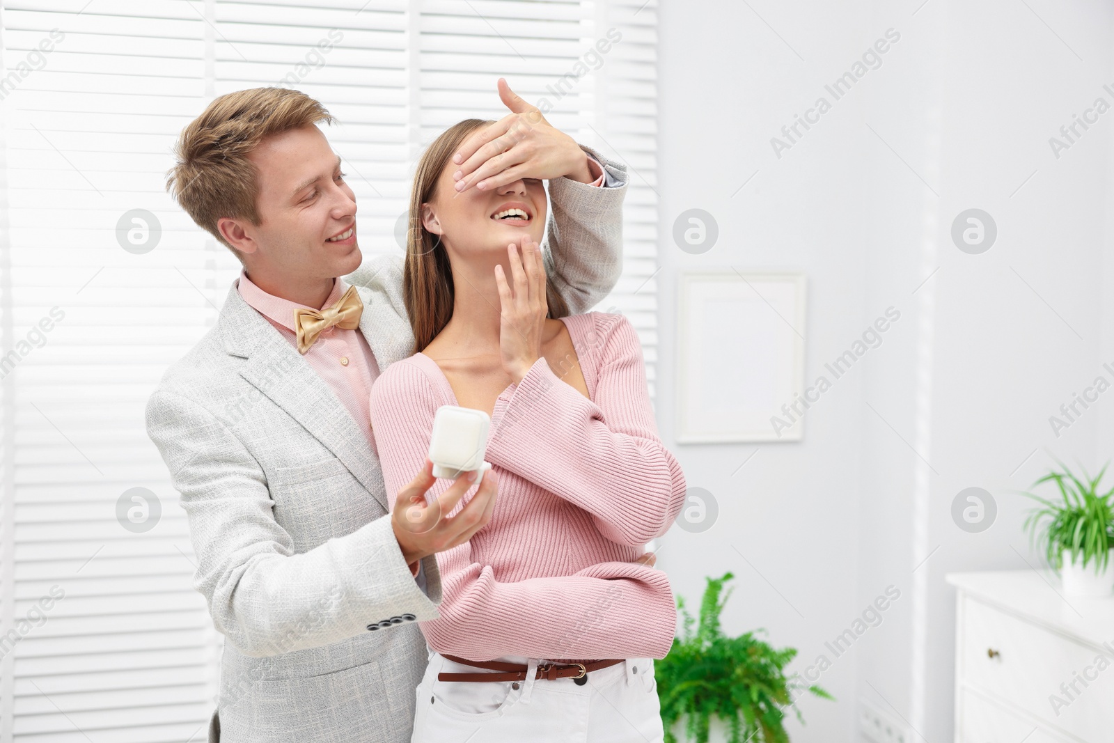 Making marriage proposal. Smiling man with engagement ring surprising his girlfriend in light room, space for text Photo of Making marriage proposal. Smiling man with engagement ring surprising his girlfriend in light room, space for text