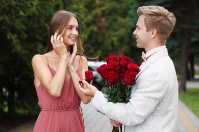 Photo of Man with engagement ring and bouquet of roses making marriage proposal to his smiling girlfriend outdoors
