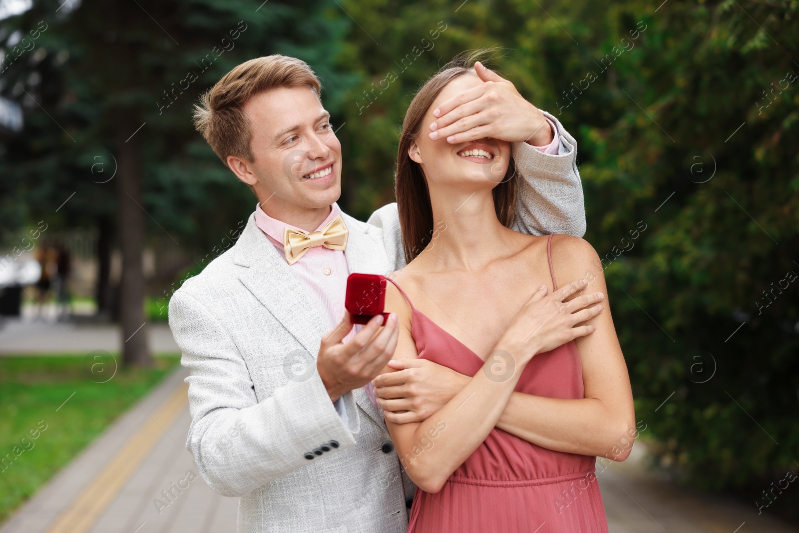 Making marriage proposal. Smiling man with engagement ring surprising his girlfriend outdoors Photo of Making marriage proposal. Smiling man with engagement ring surprising his girlfriend outdoors