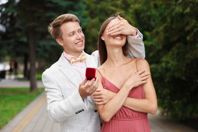 Photo of Making marriage proposal. Smiling man with engagement ring surprising his girlfriend outdoors