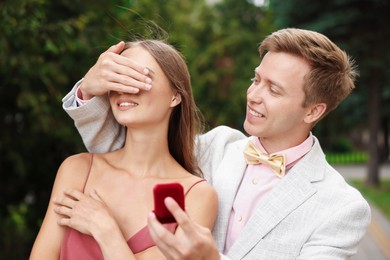 Photo of Making marriage proposal. Smiling man with engagement ring surprising his girlfriend outdoors