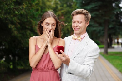 Photo of Smiling man with engagement ring making marriage proposal to his surprised girlfriend outdoors