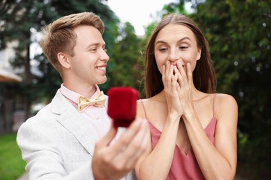 Photo of Smiling man with engagement ring making marriage proposal to his surprised girlfriend outdoors